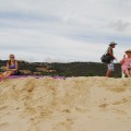 Dziewczyny siedzą na plaży, a chłopak zachęca ich do skorzystania z masażu