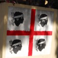 Flaga Sardynii to białe tło przedzielone czerwonym krzyżem na 4 części. W każdej z tych części umieszczona jest czarna głowa postaci z białą opaską na czole.